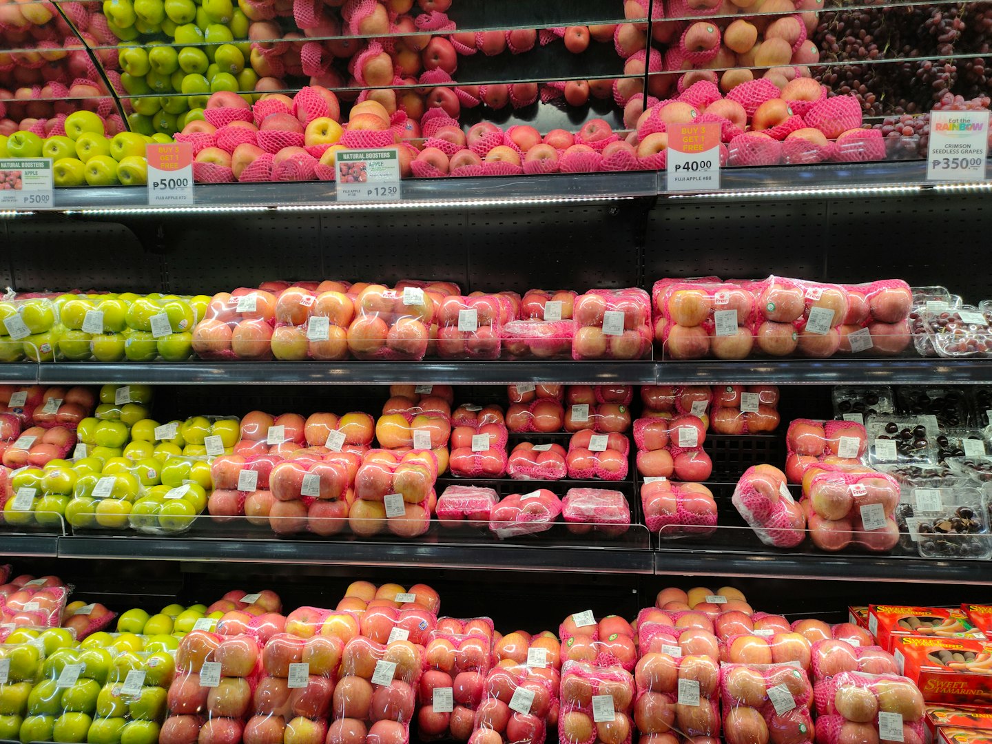 Fresh apples and grapes neatly stacked on supermarket shelves.